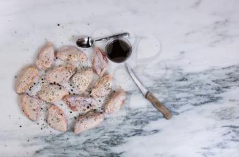 Overhead view of raw chicken wings with cooking materials and spices on natural marble stone countertop