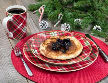 Close up view of a festive Christmas breakfast meal and coffee with evergreen branches on top of rustic wood. 