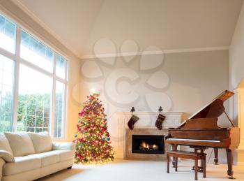 Christmas tree in living room with burning fireplace and grand piano during bright day time.