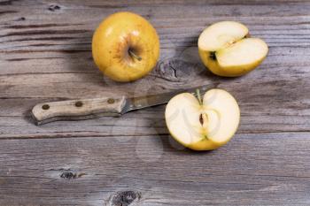 Selective focus on sliced golden apple with paring knife and whole apple in background on rustic wooden boards