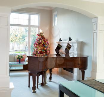 Living room entrance with grand piano, decorated Christmas tree and large daylight window in background 