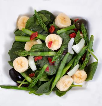 Fresh salad with spinach, asparagus, olive, banana, onion, olives, and cranberries. Close up overhead view. 