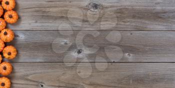 Left border of small pumpkins on rustic wooden boards for Autumn holiday background
