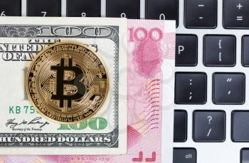 Gold Bitcoin with mixed paper currency and computer keyboard in background