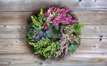 Colorful artificial wreath made of flowers and leaves on vintage wood background 