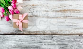 overhead view of a pink springtime tulips and brown gift box on white weathered wooden boards 