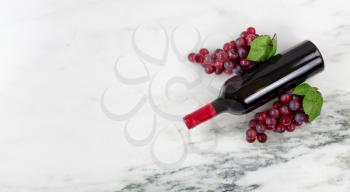 Overhead view of Red wine bottle with grapes on natural marble stone setting