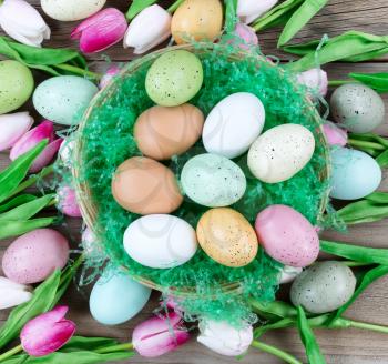 Small basket filled with colorful eggs and pink tulips on weathered wooden boards for Easter background  