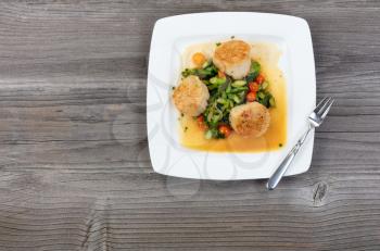Top view of freshly cooked scallops with vegetables on rustic wooden table 