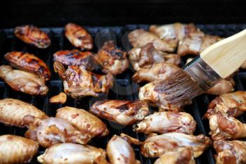 Close up of an open barbecue grill cooking chicken wings while being brushed with spicy sauce   