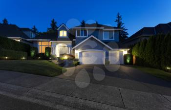 Modern suburban home exterior on a late summer evening with lights on yard and house 