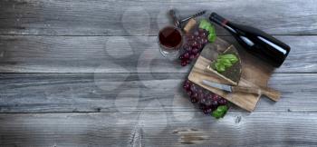 Red wine with fresh cheese wedge plus basil leaves and grapes on rustic wood with copy space available 