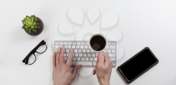 Office desk table with male hands holding cup of coffee over computer keyboard while working. Overhead with copy space available in flat lay format. 