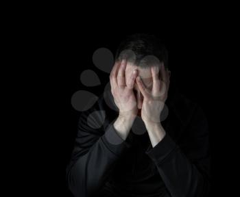 Depressed mature man with face down in both hands while surrounded by darkness 