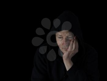 Depressed mature man holding his chin in the darkness while dressed in a black hooded sweater 