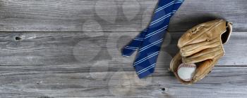 Blue striped necktie and a baseball glove with ball on weathered wooden planks for Happy Fathers Day concept 