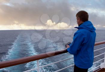 Mature man wearing rain jacket while looking from stern of boat out into sea 