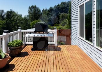Outdoor BBQ cooker with lid open displaying smoke coming out while on home wooden deck during summertime 