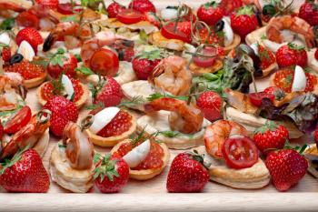 Lot of canape with  shrimp, caviar, strawberries and other on wooden tray, selective focus