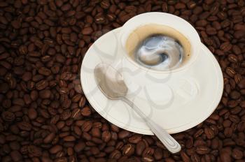 cup of coffee with teaspoon on coffee beans background