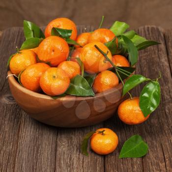 Fresh tangerines with leaves in bowl on wooden table. Closeup.