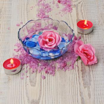 Soap in form of roses in bowl of water on wooden background. Closeup.