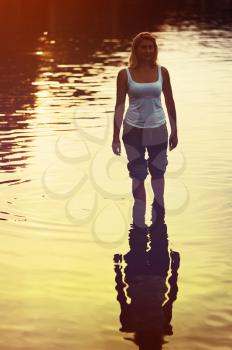 Lovely woman in jeans rolled in sea water on soft background of setting sun with retro effect filter.