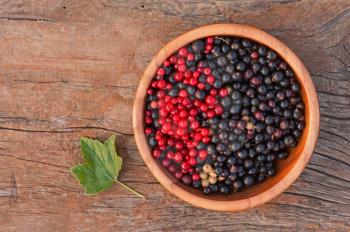 Sweet, black and red currant and green leaves in wooden bowl. Closeup. Selective focus.