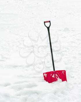 Red plastic shovel with black handle stuck in fluffy white snow.