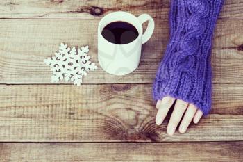 Woman hand in teal glove, mug with hot coffee or cocoa and snowflake on wooden background.  Winter and Christmas concept.