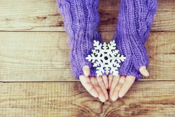 Woman hands in light teal knitted mittens are holding snowflake on wooden background. Winter and Christmas concept.