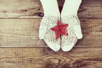 Woman hands in light teal knitted mittens are holding red snowflake on wooden background. Winter and Christmas concept.