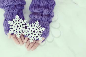 Woman hands in light teal knitted mittens are holding snowflakes on snow  background. Winter and Christmas concept.