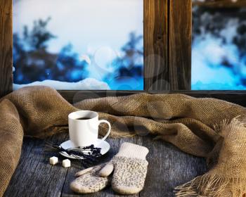 White cup of coffee or tea, lavender flowers, mittens and natural gunny cloth located on stylized wooden window sill. Winter concept of comfort and relaxation.