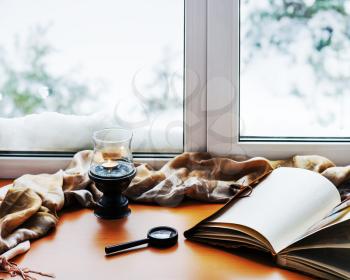 Open photo album, candle, magnifying glass and and beige warm plaid located on a stylized wooden windowsill. Winter concept of comfort and relaxation.
