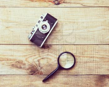 Vintage, very old film camera and magnifying glass on brown wooden background and space for text. Photo with retro filter effect.
