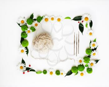 Skein of wool and hooks knitting with decoration of chrysanthemum flowers and ficus leaves on white background. Overhead view. Flat lay.