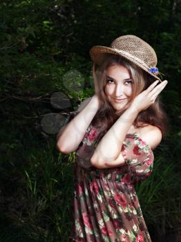 Beautiful blonde girl with long hair in national dress and hat standing in forest.