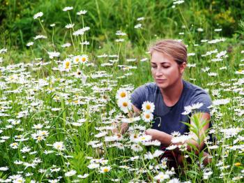 Beautiful young woman sitting on flowering meadow with daisies.