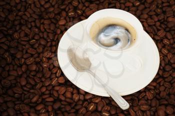Cup of coffee with teaspoon on coffee beans background. 