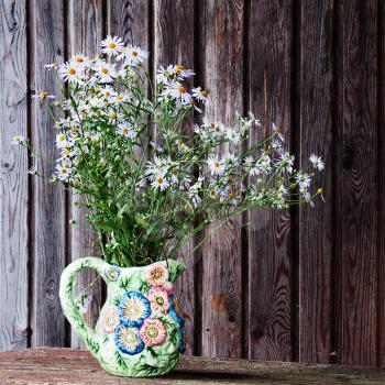 Still life with blue asters in vase on wooden background.