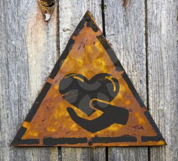Royalty Free Photo of a Hand Holding a Heart on a Rusty Sign Against a Wooden Wall