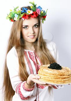 Ukrainian woman in a wreath holds pancakes with caviar