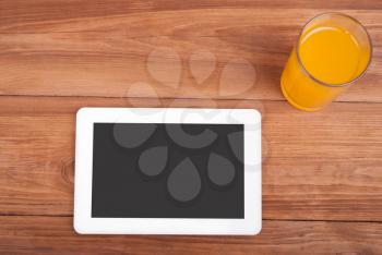 Digital tablet and a glass of orange juice on a wooden table.