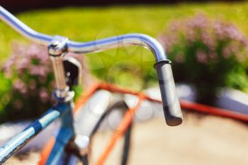 Vintage Bicycle Handlebar Detail Close Up With Parking Bokeh Background In Flower Bed In Sunny Day