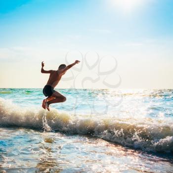 Boy Jumping In Sea Waves. Jump Accompanied By Water Splashes. Summer Sunny Day, Ocean Coast