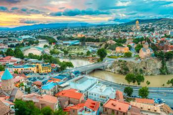 The Scenic Top View Of The Central Part Of Summer Tbilisi, Georgia With All Famous Landmarks, Sightseeings, Kura Mtkvari River Under Bridges, The Beautiful Sunset Sunrise Dawn Sky Above.