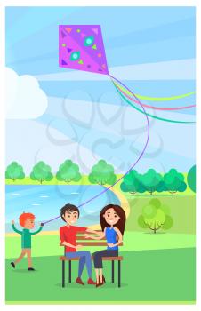 Young couple sitting on wooden bench in public park and running little boy that flies kite near lake on background. Relaxation outdoors in summer
