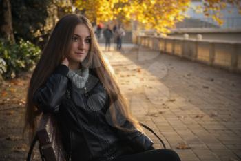 young beautiful girl with long hair on the bench autumn day in the Park on a background of yellow leaves lit by the sun