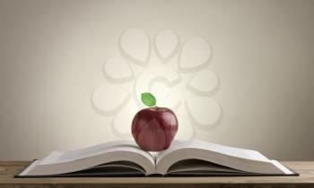 open book on a wooden Desk with a red Apple and green leaves on a grey-lit background. open book on a wooden Desk with a red Apple